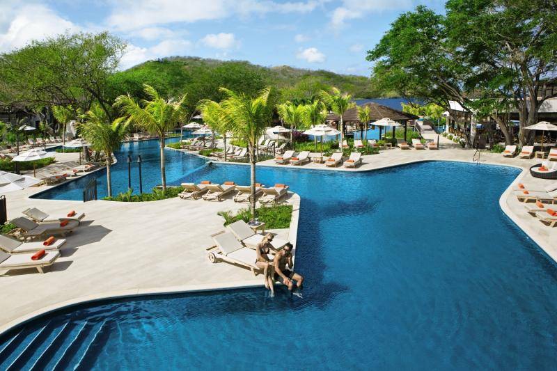 Poolbereich im Dreams Las Mareas Costa Rica mit zwei Personen, die ins Wasser springen.