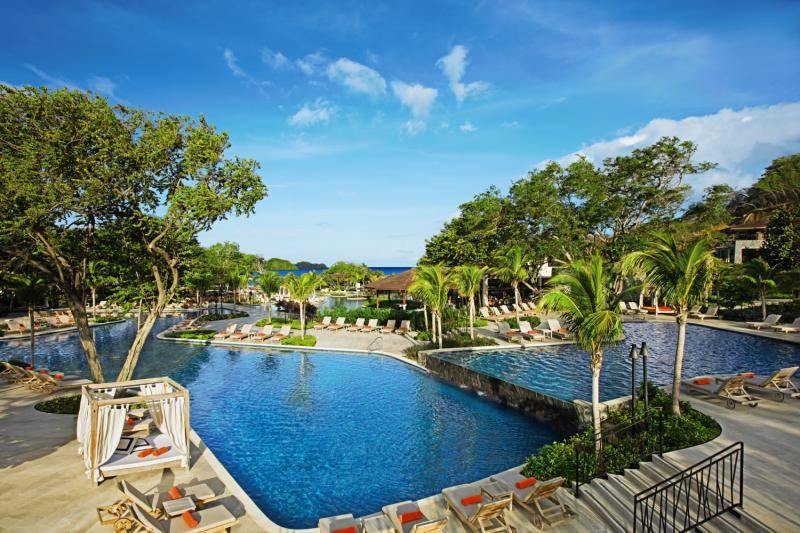 Außenpool im Dreams Las Mareas Costa Rica Resort mit Loungeliegen und Palmen.