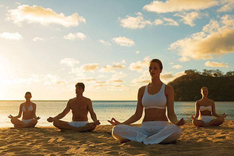 Vier Personen praktizieren Yoga auf einem Strand bei Sonnenuntergang.