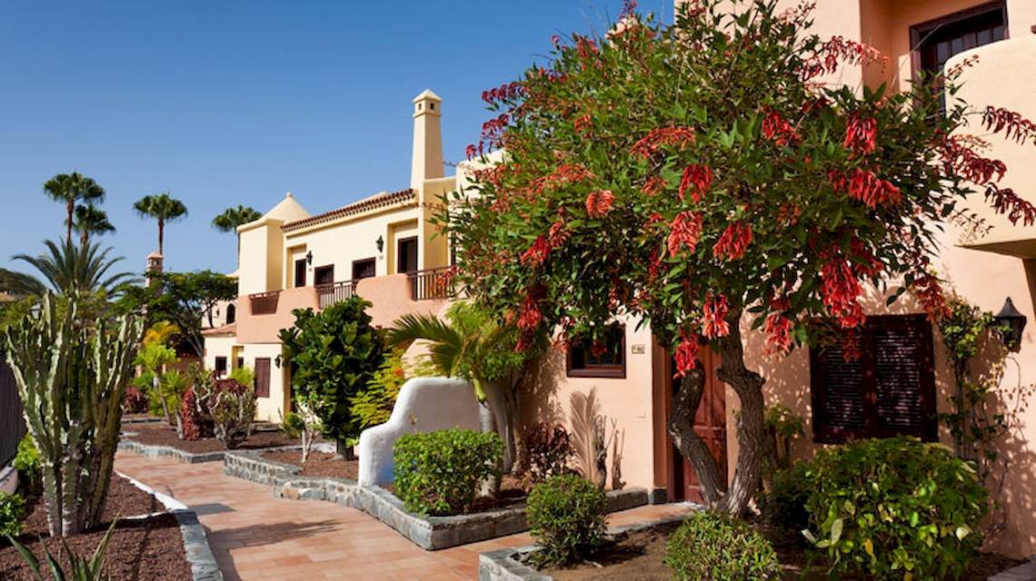 Außenansicht des Tagoro Family & Fun Costa Adeje Hotels mit Gehweg, Bäumen und Pflanzen.
