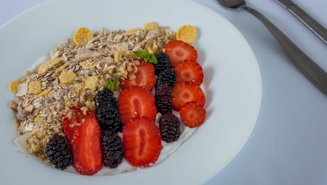 Ein weißer Teller mit Müsli, frischen Früchten und Kokosflocken.