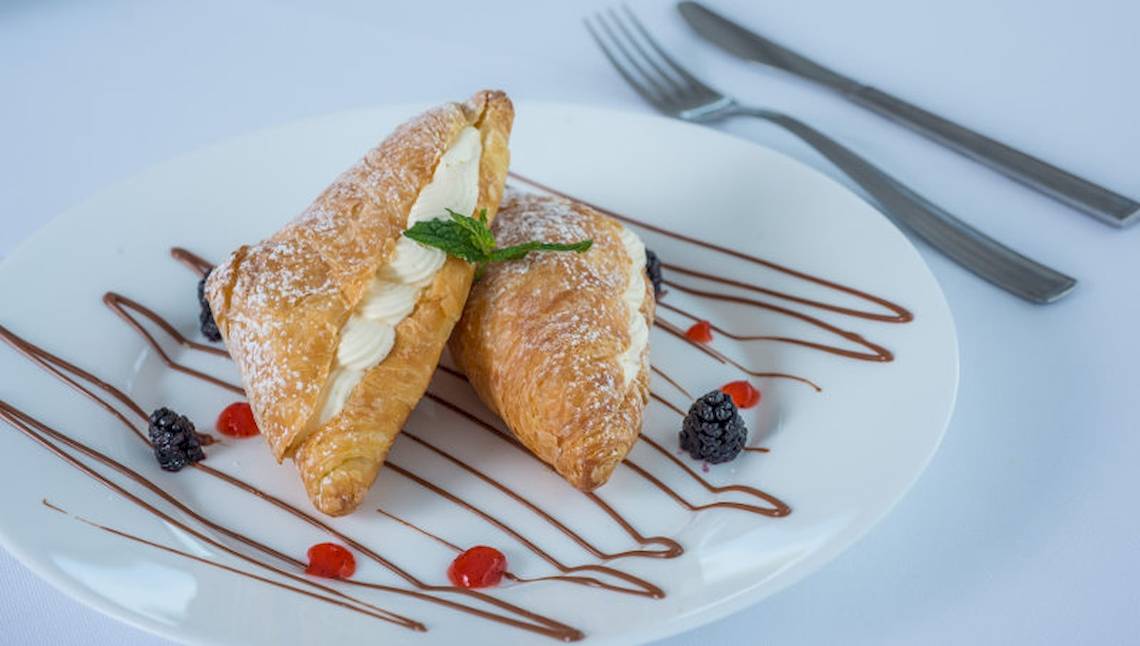 Zwei Croissants mit Sahne und Beeren auf einem weißen Teller mit Schokoladensauce und Minzblatt.