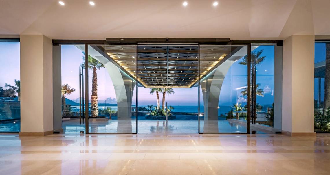 Glasfluegeltuere und lobby des mitsis rodos village beach hotel mit ausblick auf meer und palmen
