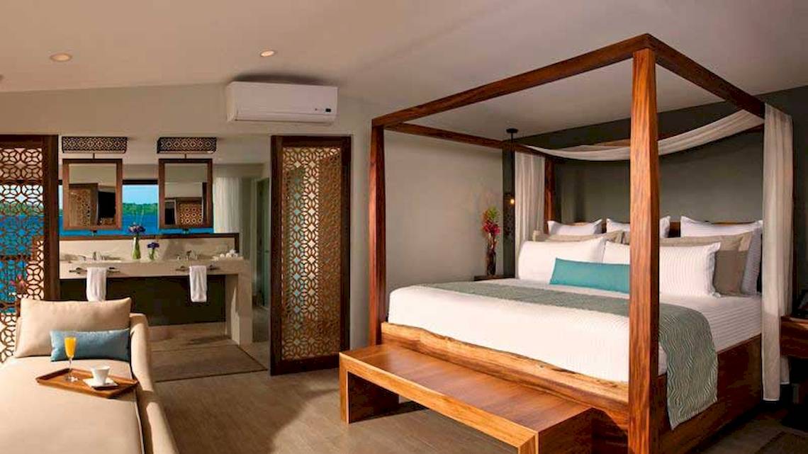 Luxuriöses Hotelzimmer im Secrets Papagayo Costa Rica mit Baldachinbett, Sofa und Badezimmer mit Badewanne.