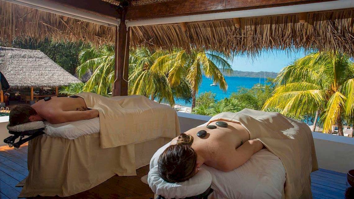 Zwei Personen erhalten eine Massage mit heißen Steinen auf einer Terrasse mit Blick auf das Meer im Hotel Secrets Papagayo Costa Rica.