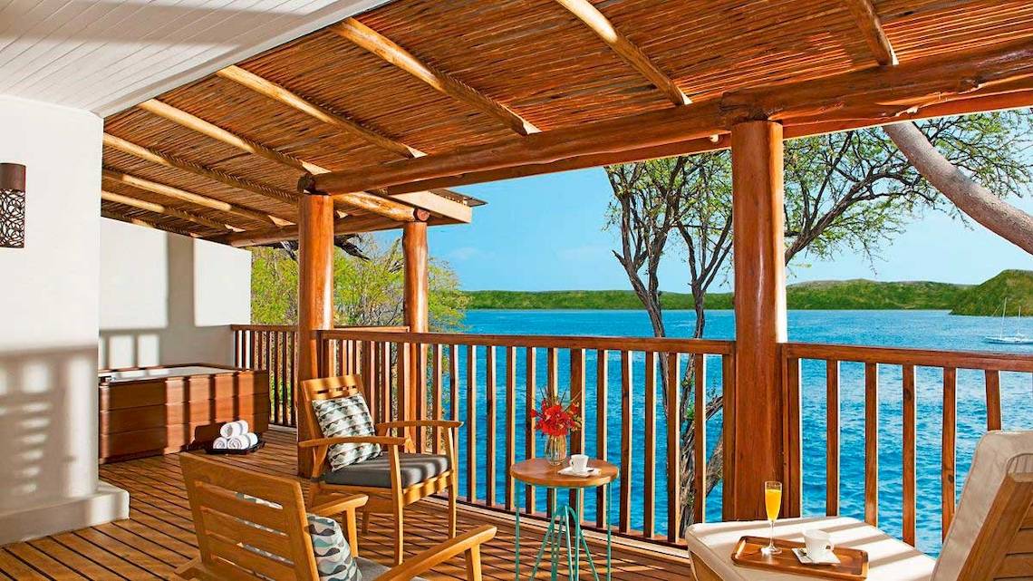 Balkon mit Meerblick im Secrets Papagayo Hotel, Costa Rica, mit Holzmöbeln, einem kleinen Tisch und Ausblick auf das Meer.