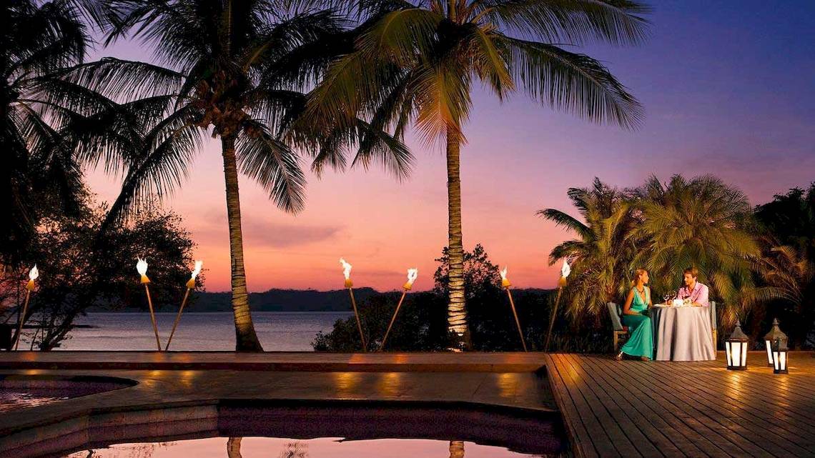 Ein Paar genießt ein Abendessen am Swimmingpool im Secrets Papagayo Hotel bei Sonnenuntergang.