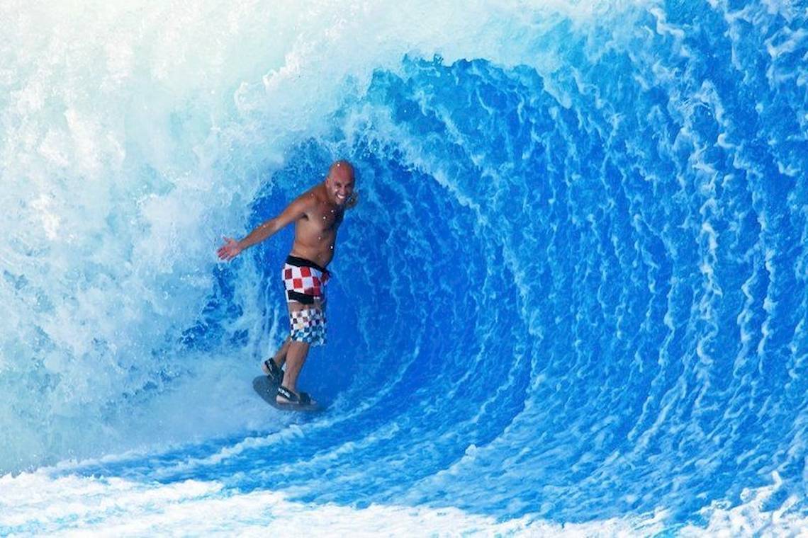 Ein Mann surft in einer großen blauen künstlichen Welle in einem Wasserpark.