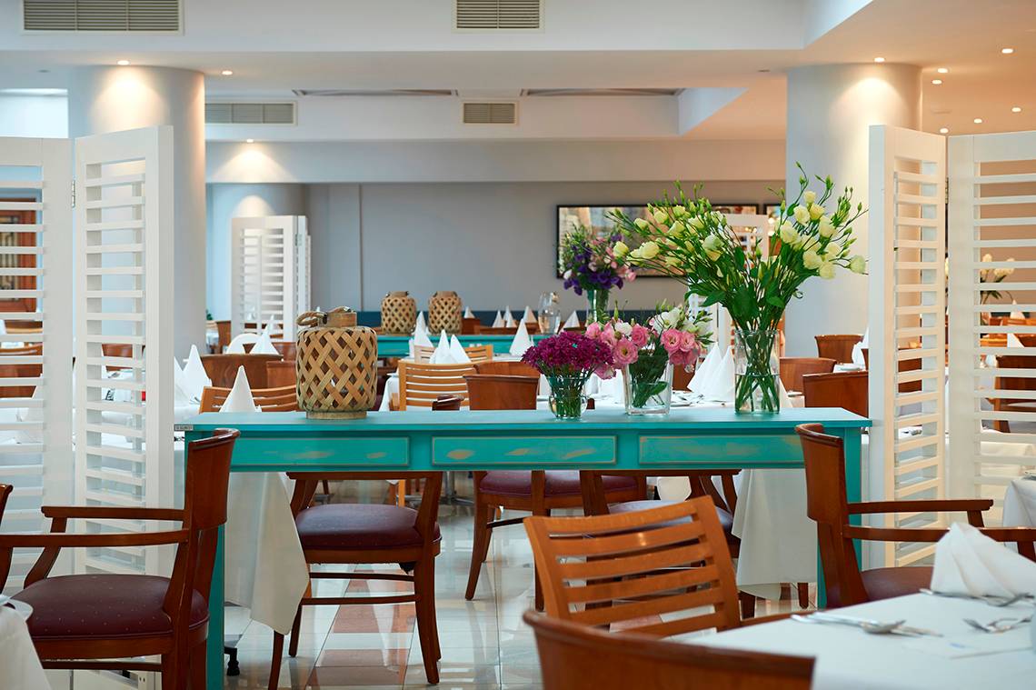 Innenansicht des Restaurants im Louis Ledra Beach Hotel mit blauem Tisch und Blumenvasen.