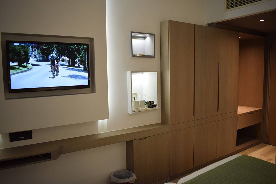 Zimmer im Minos Mare Hotel mit Fernseher und Schrank, der an die Wand montiert ist.