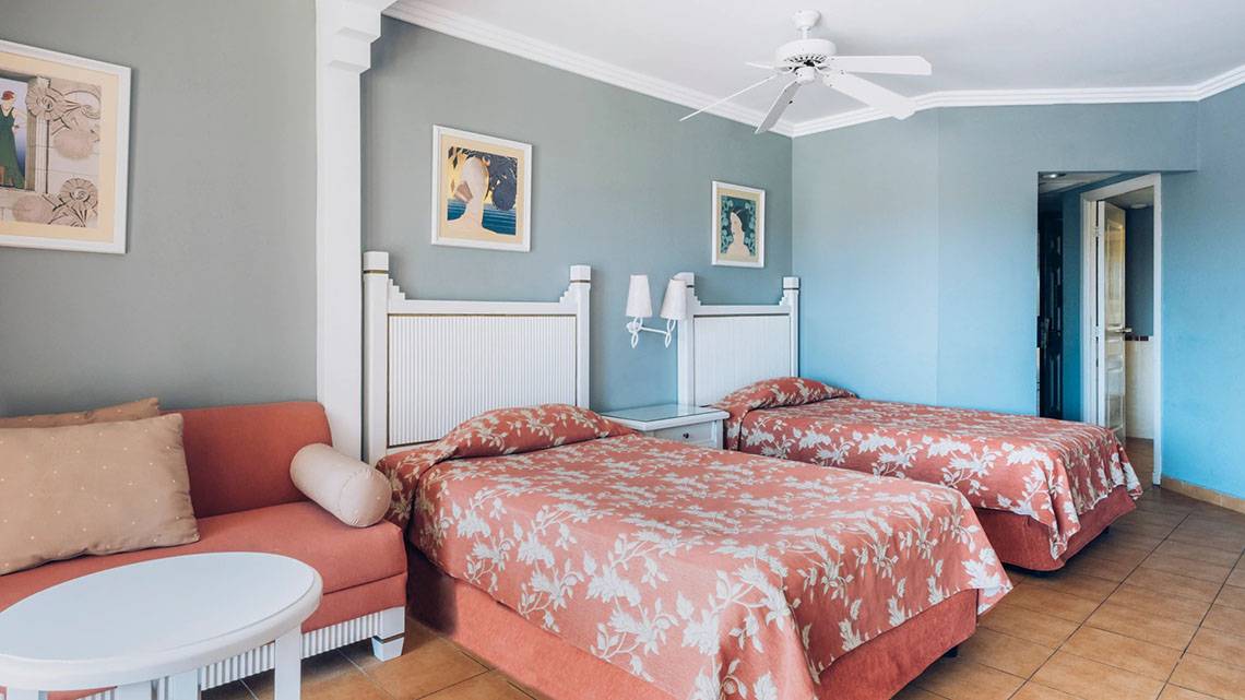 Doppelzimmer im Iberostar Laguna Azul Hotel mit zwei Betten, Couch, Nachttisch und Deckenventilator.