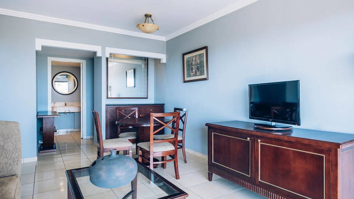 Wohnzimmer des Iberostar Laguna Azul Hotels mit Fernseher, Esstisch und Stühlen.