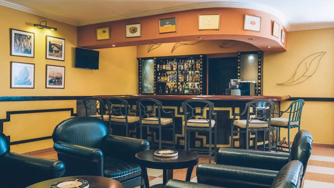 Barbereich im Hotel Iberostar Laguna Azul mit gelben Wänden, gemusterten Stühlen und einer Theke mit vielen Flaschen.