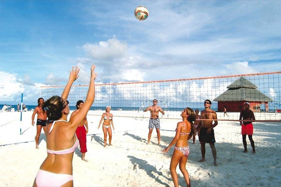 Gruppe von Leuten spielt Volleyball auf dem Strand mit einem Netz und einem Ball in der Luft.