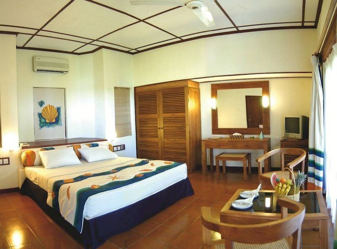 Ein Schlafzimmer im Adaaran Club Rannalhi Hotel mit einem Bett, Möbeln und einer Klimaanlage.