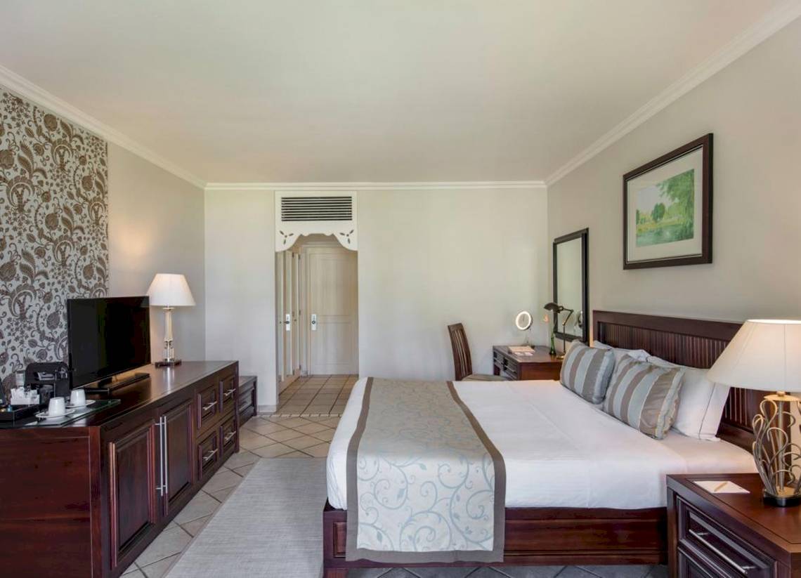 Ein elegantes Hotelzimmer im Sugar Beach Mauritius mit einem großen Bett, Fernseher, und Nachttischen.