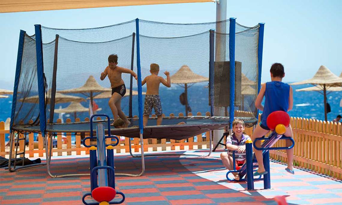 Kinder spielen auf einem Trampolin und anderen Spielgeräten am Strand, mit Blick auf das Meer.