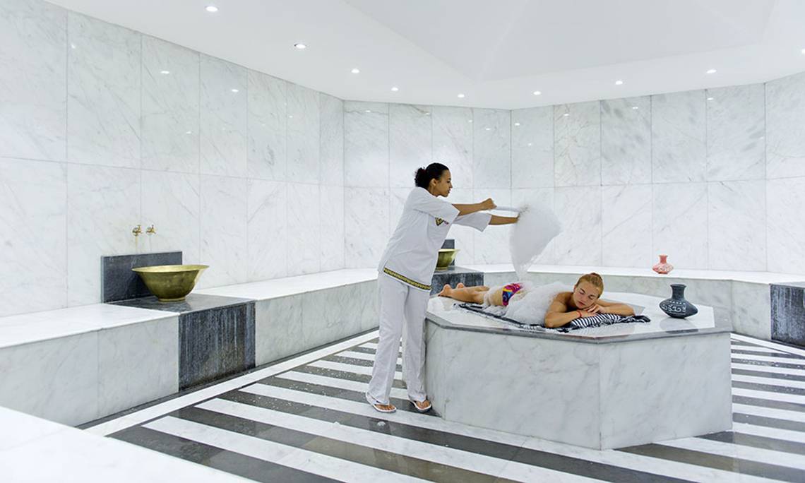 Eine Frau im weißen Outfit serviert einem Gast im Whirlpool im Spa-Bereich des Amphoras Beach Hotels.