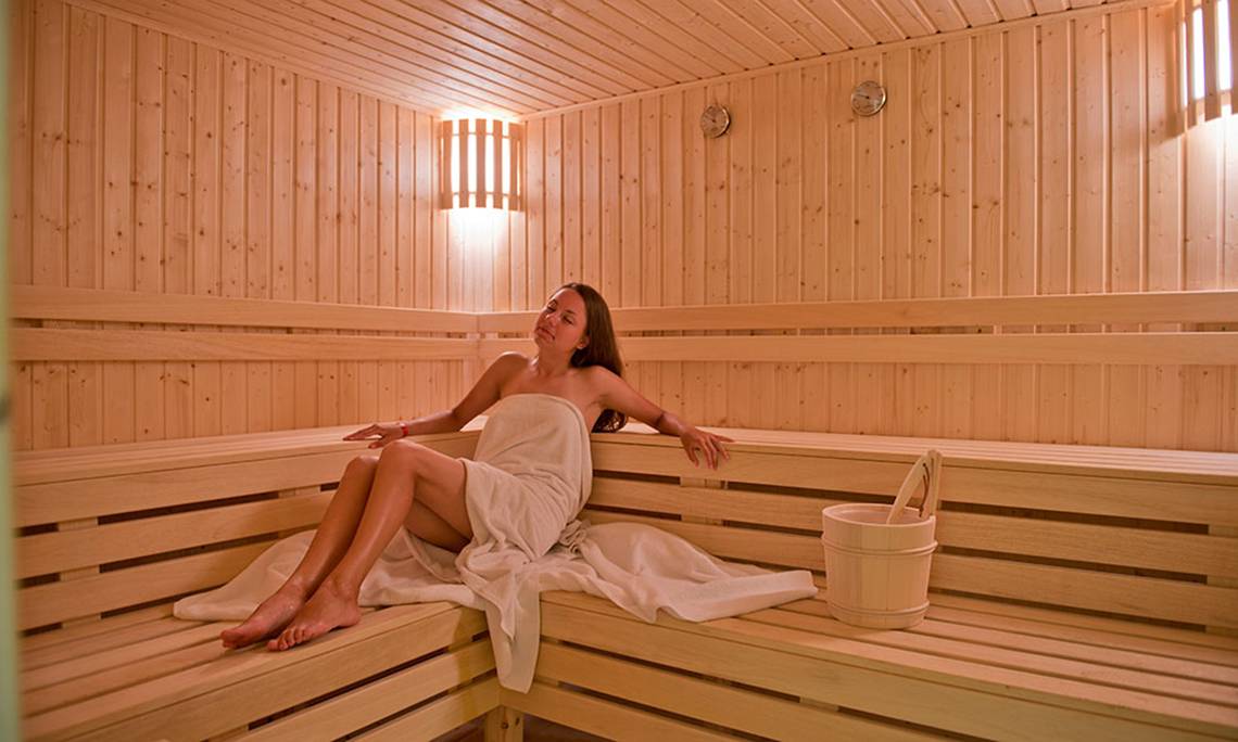 Eine Frau sitzt in einer Sauna des Amphoras Beach Hotels und hält einen Handtuch.
