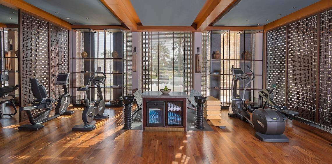 Fitnessbereich im Hotel Chedi Muscat mit Geräten und Fenstern.