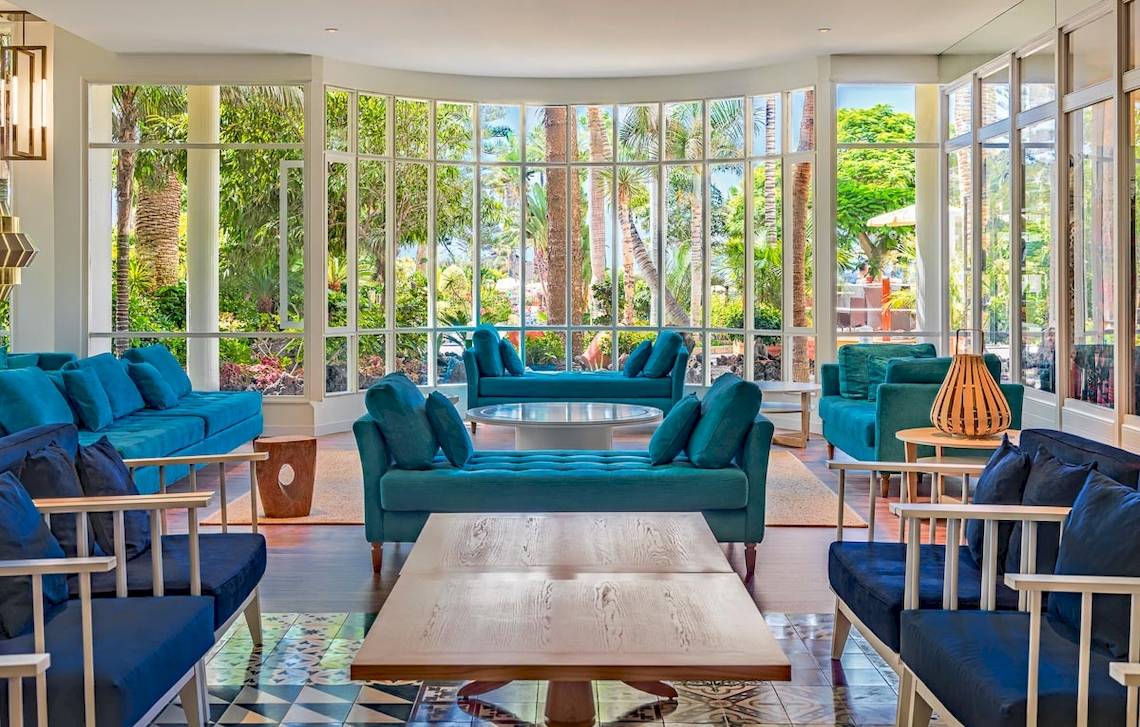 Lobby des H10 Las Palmeras Hotels mit blauen Sofas, runden Tischen und großen Fenstern.