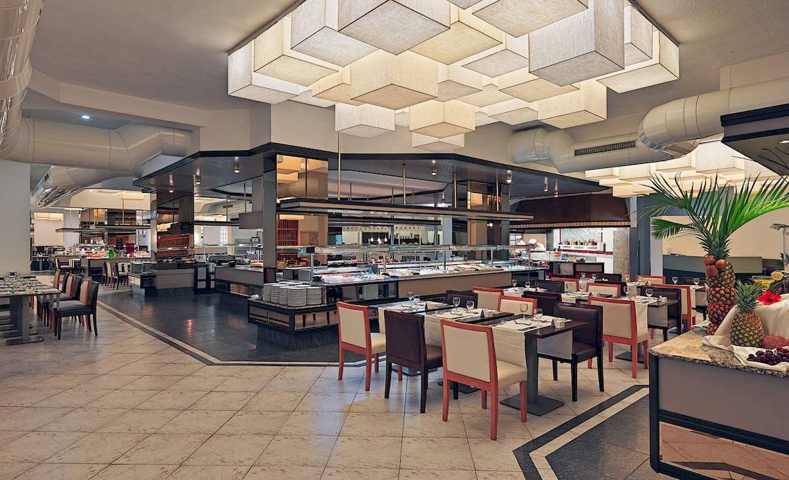 Innenansicht des Restaurants des H10 Las Palmeras Hotels mit geometrischen Deckenleuchten, Buffet und gedeckten Tischen.