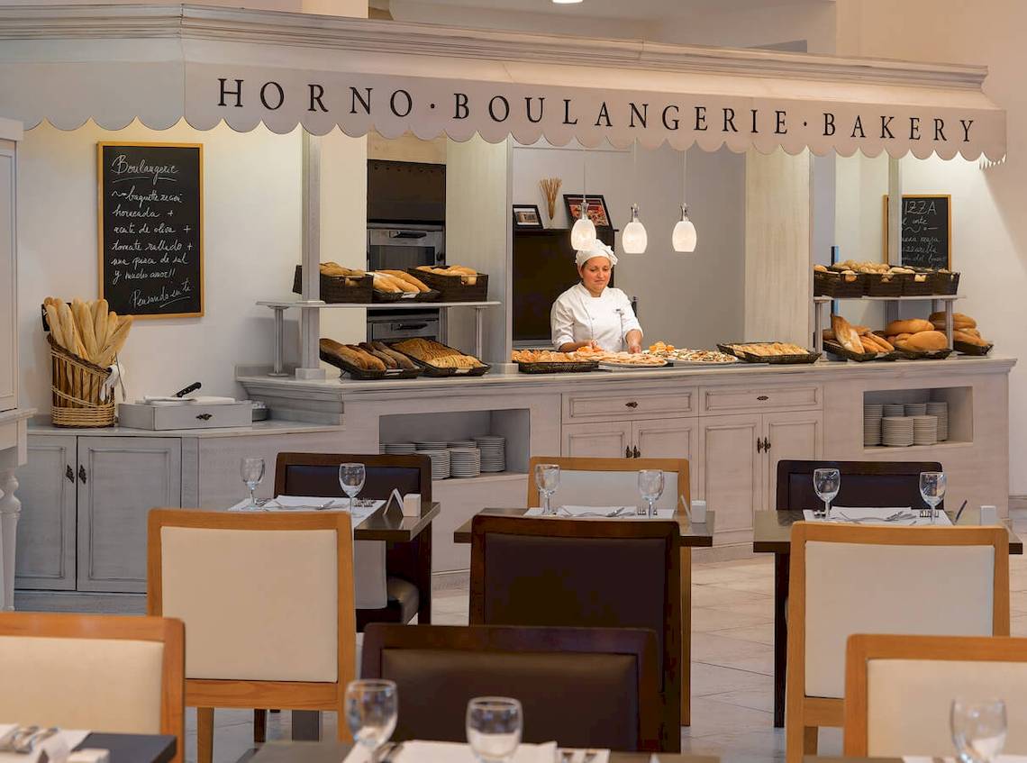 Eine Bäckerei im H10 Las Palmeras Hotel mit einer Köchin, die Gerichte serviert.