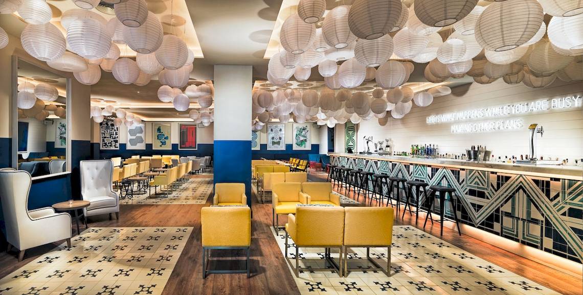 Loungebereich des H10 Las Palmeras Hotels mit gelben Sesseln, weißen Lampions und einer Theke.