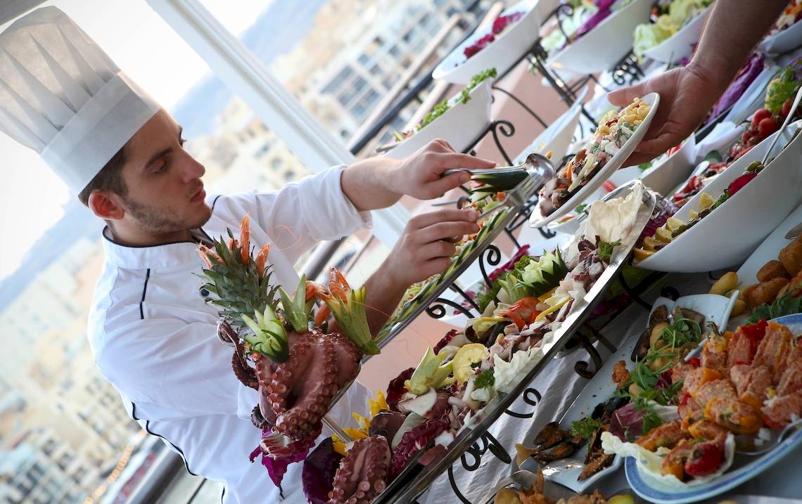 Koch beim Calypso Hotel bereitet ein Buffet auf einem Tisch mit verschiedenen Gerichten vor.