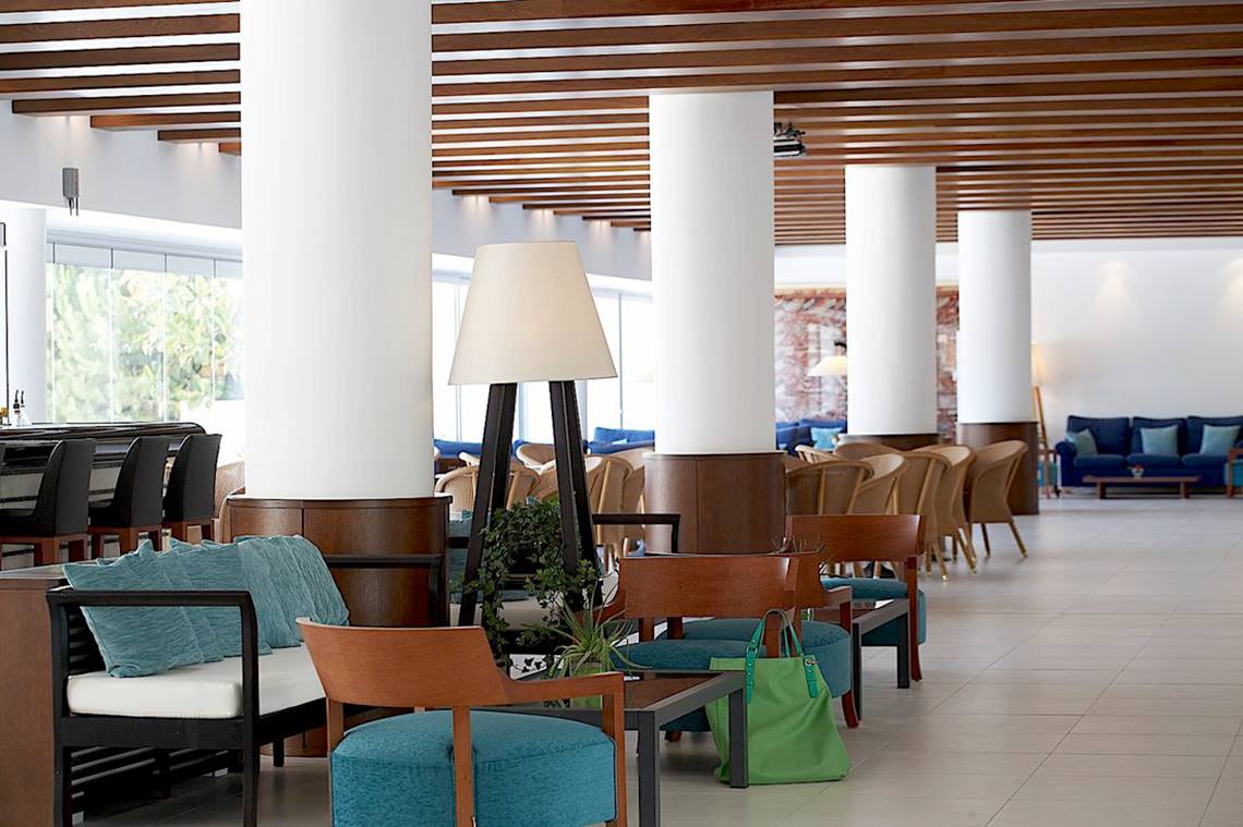 Lobbybereich des Cretan Malia Park Hotels mit Sitzmöbeln, einer Stehlampe und weißen Fliesen.