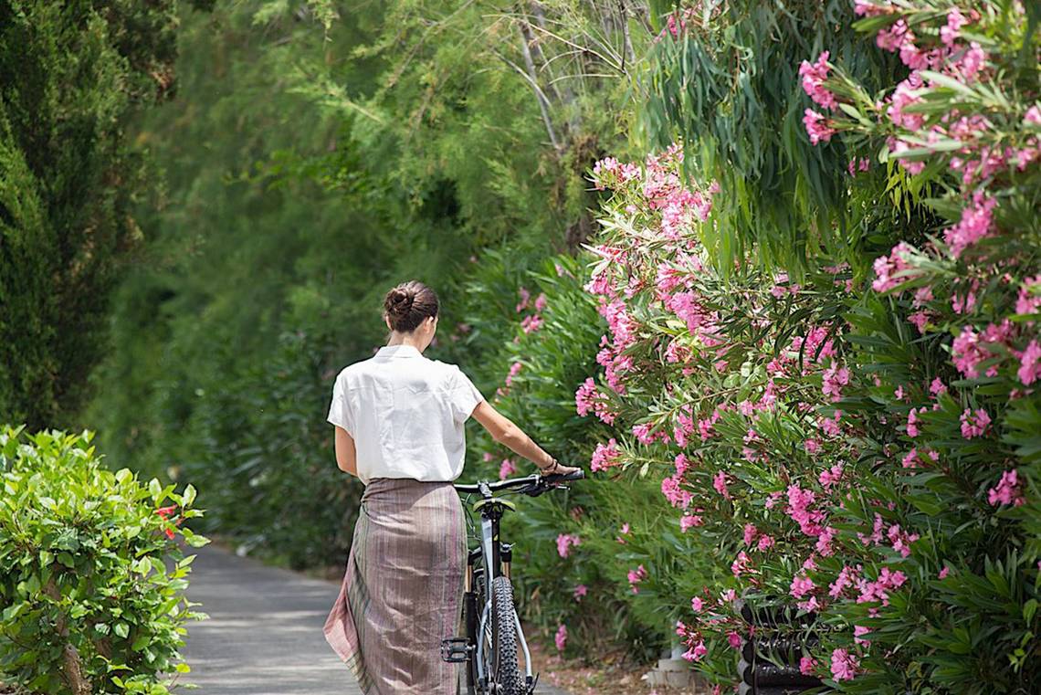 Frau mit Fahrrad am Cretan Malia Park entlang des Weges mit rosa Blumen