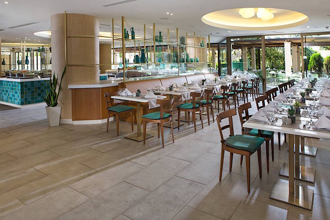 Innenansicht des Restaurants im Cretan Malia Park Hotel mit gedeckten Tischen und Stühlen.
