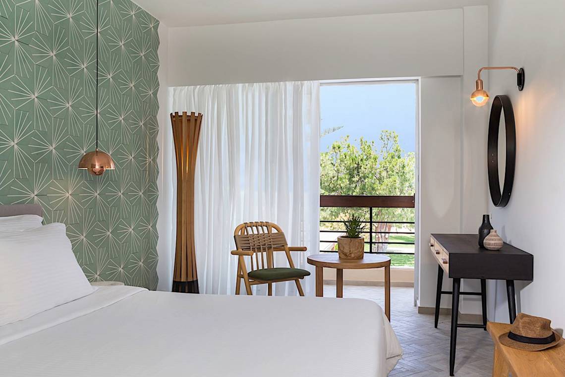 Ein elegantes Bettzimmer im Cretan Malia Park Hotel mit einem Balkon und grünen Wänden.