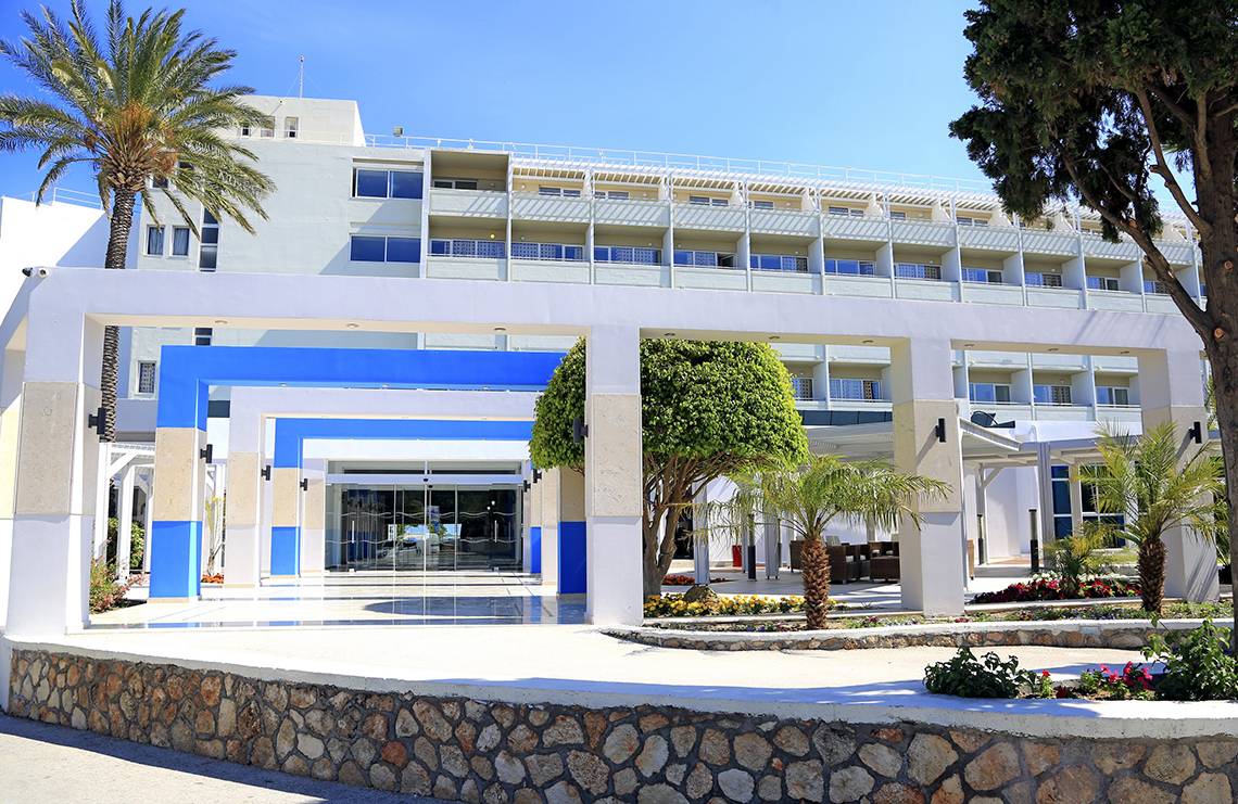 Vorderansicht des Blue Bay Beach Resorts mit Eingang, Säulen und Palmen