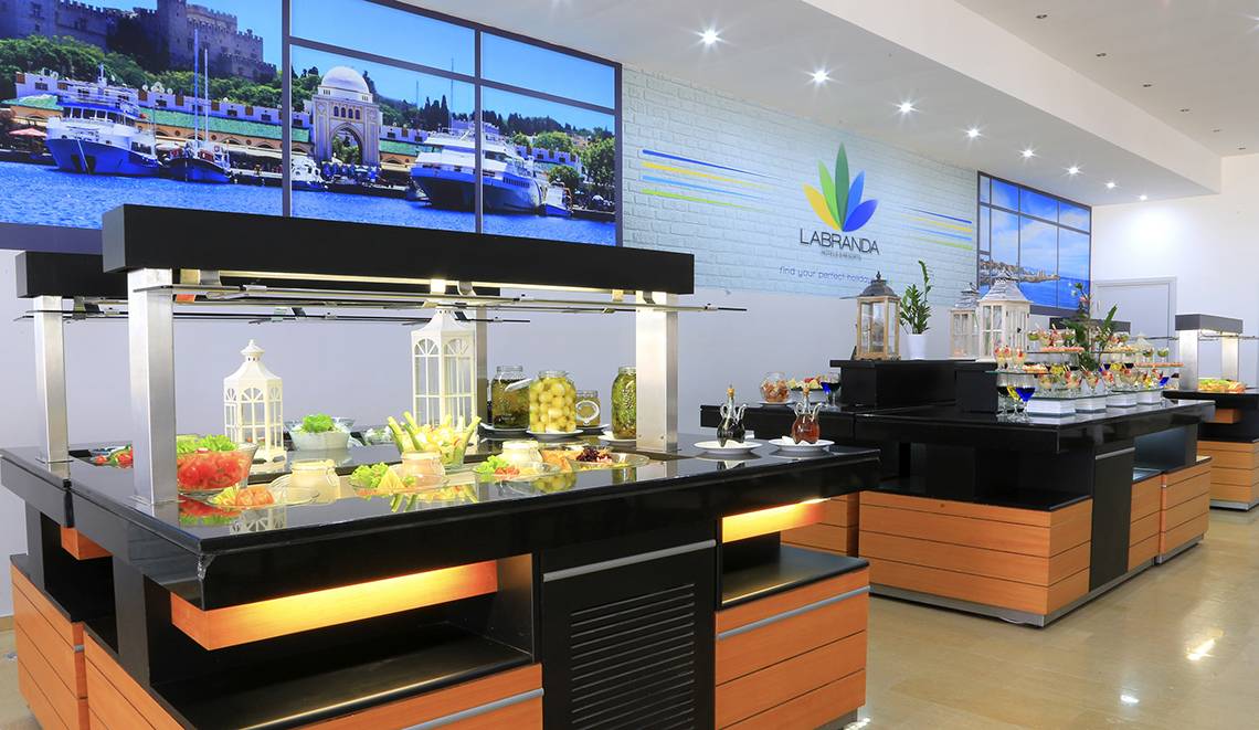 Buffetbereich im Blue Bay Beach Resort mit vielen Lebensmitteln und einer großen Fensterwand.