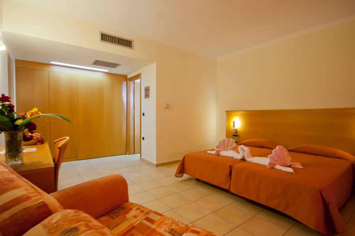 Zimmer im Tigaki Beach Hotel mit zwei Betten und einer Couch, umgeben von Dekoration.