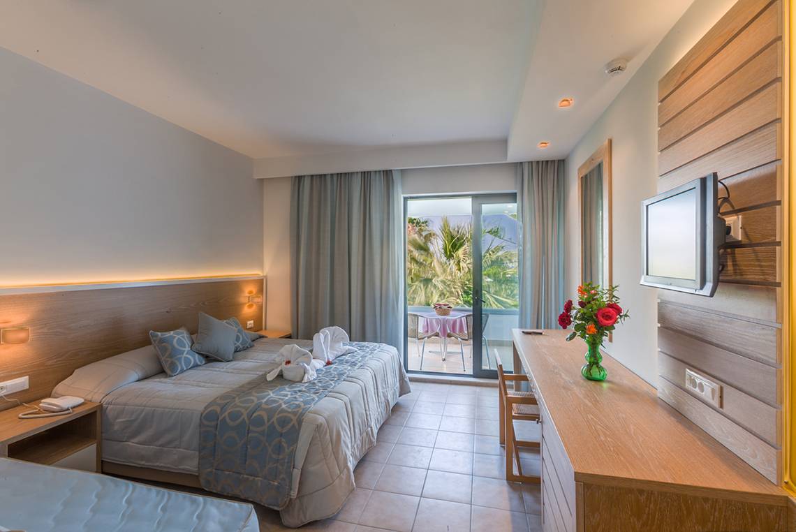 Ein elegantes Zimmer im Tigaki Beach Hotel mit zwei Betten, einem Schreibtisch und einem Balkon.