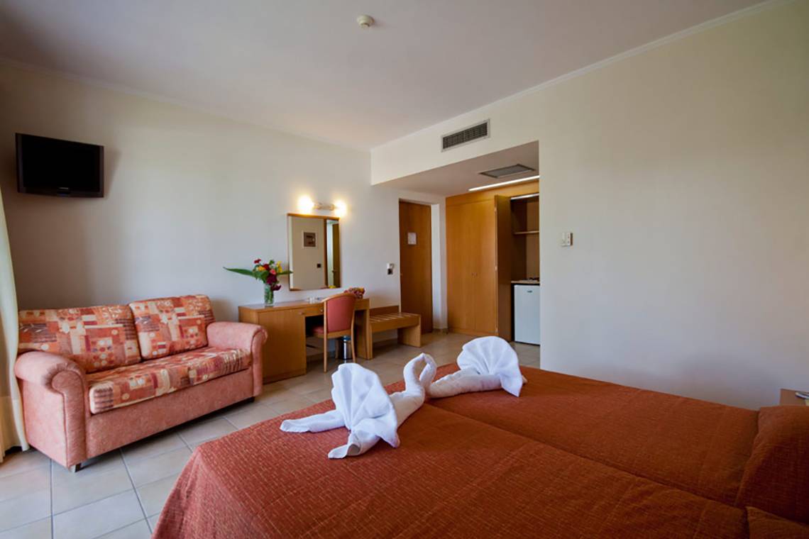 Zimmer im Hotel Tigaki Beach mit Bett, Sofa, Schreibtisch und Fernseher.