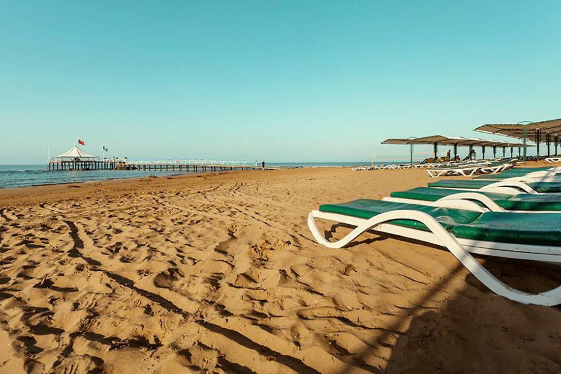 Strand des Turan Prince Hotels mit Sonnenliegen und Pier am Horizont