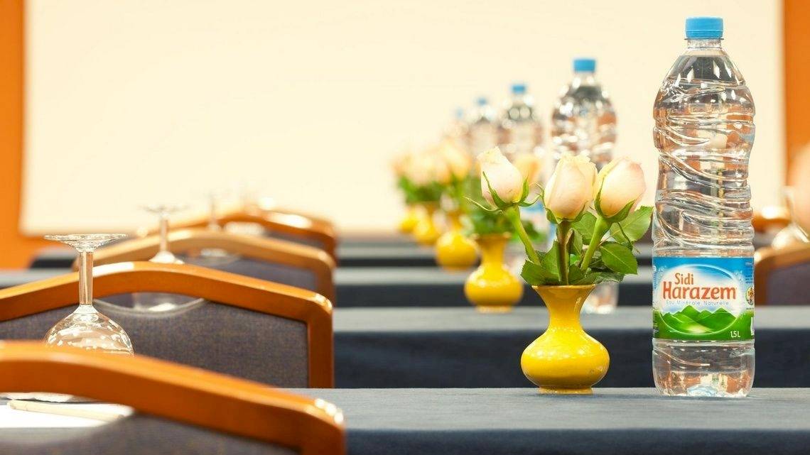Konferenzraum im Le Meridien N'Fis Hotel mit blauen Tischen, weißen Rosen in gelben Vasen und Wasserflaschen.