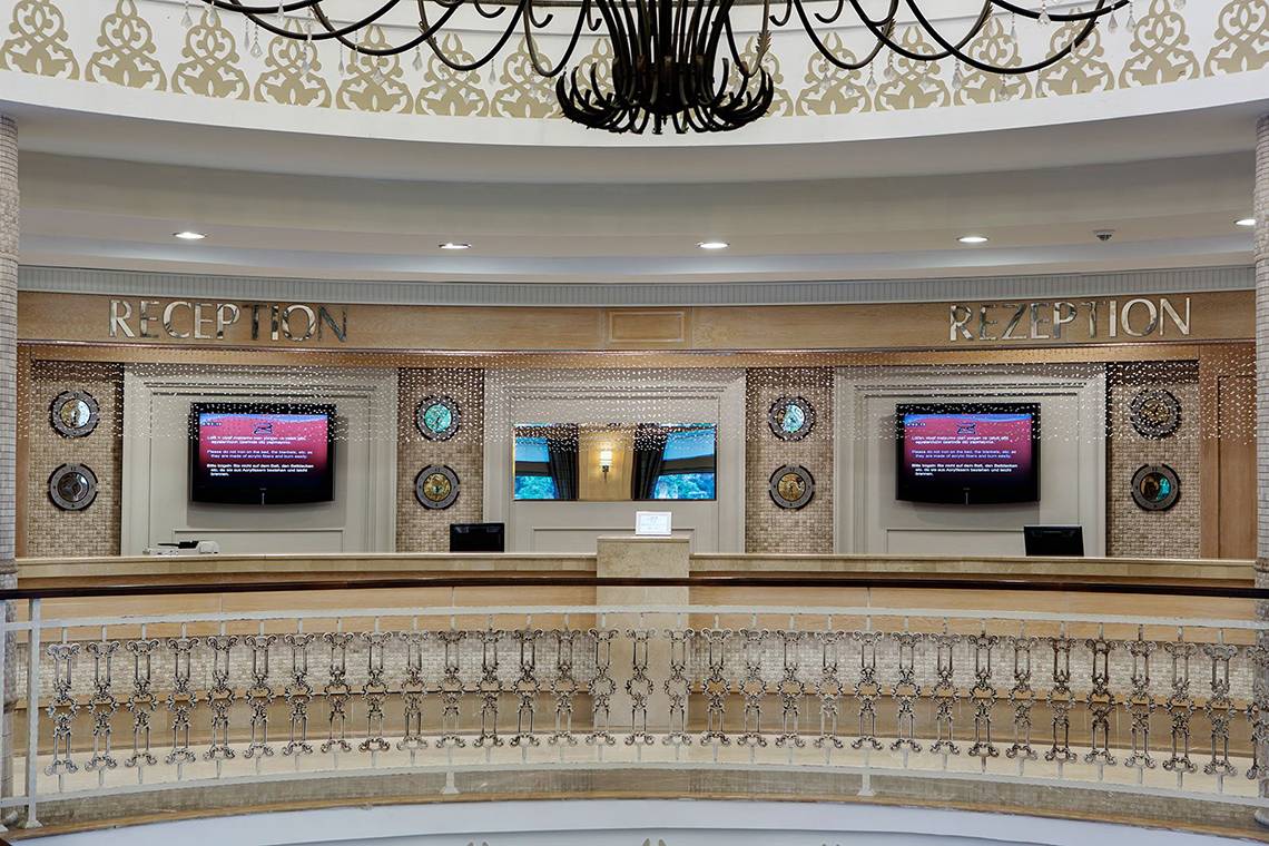 Empfangsbereich des Alba Queen Hotels mit zwei Fernsehern und einer großen Lampe.