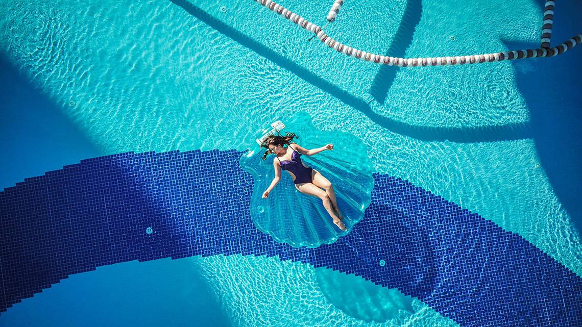 Eine Frau liegt entspannt auf einer Liege im blauen Pool des Alba Queen Hotels.