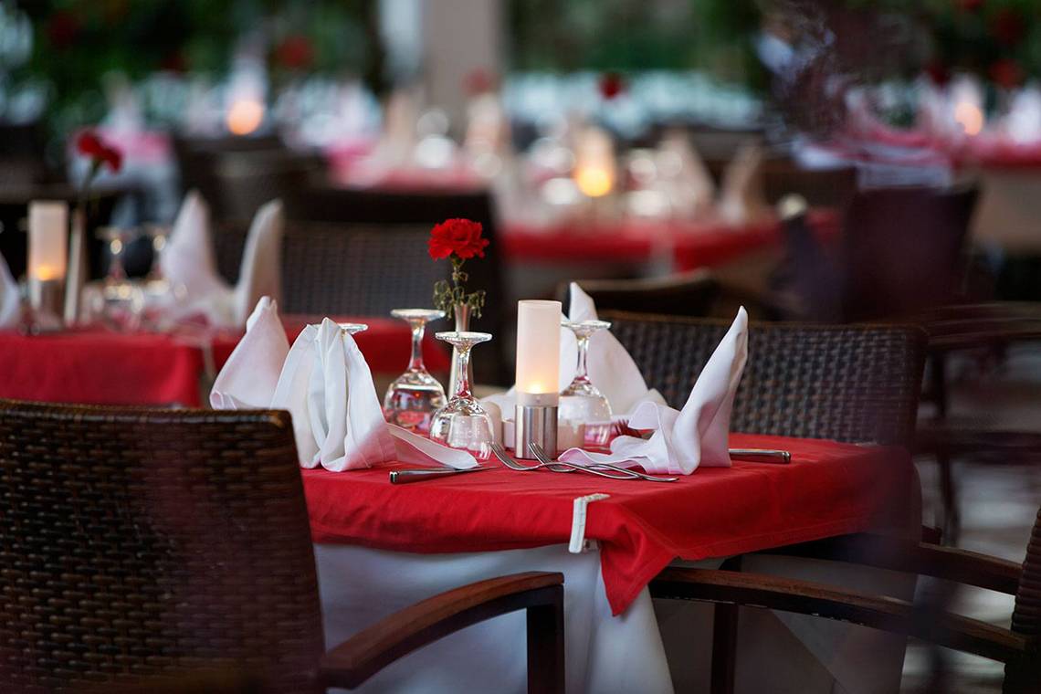 Foto von einem eleganten Hotelspeisesaal mit roten Tischdecken, Blumen und Kerzen.