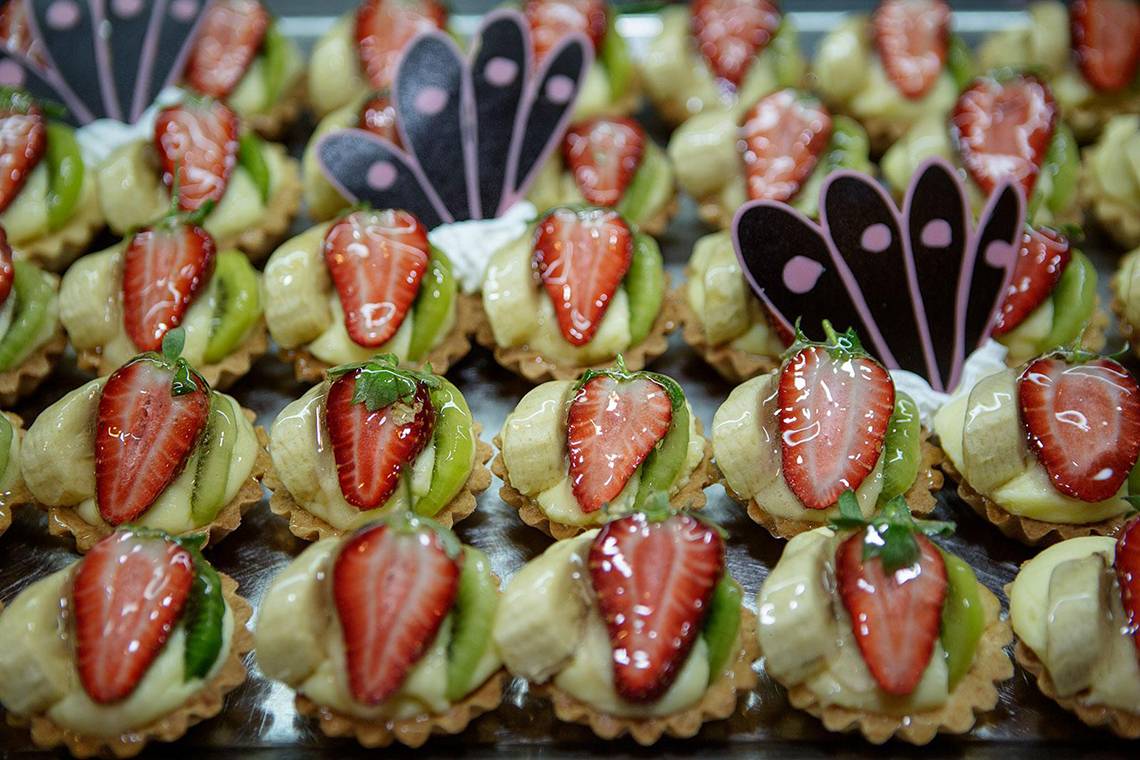 Nahaufnahme von Obstcreme-Tartes, jede mit frischen Früchten und grünen Blättern garniert.