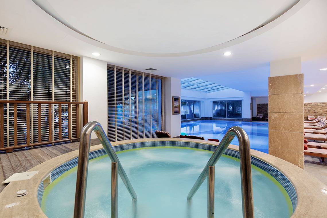 Innenpool im Alba Queen Hotel mit Blick auf den Außenpool und Sonnenliegen.
