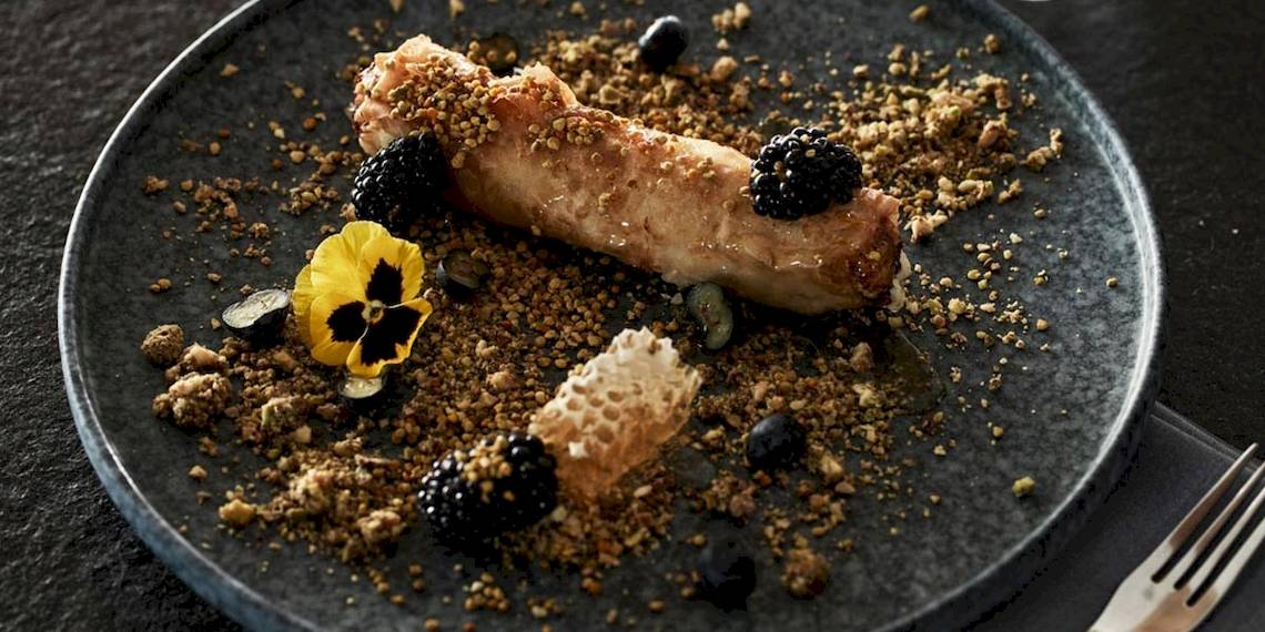 Ein Gericht auf einem Teller im Myconian Kyma Hotel, bestehend aus einem gebackenen Stück Fleisch mit Pistazien und Beeren.