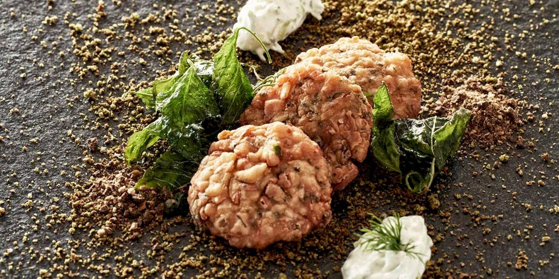 Fischkroketten von Myconian Kyma mit grünem Blattwerk und Gewürzen auf schwarzem Teller