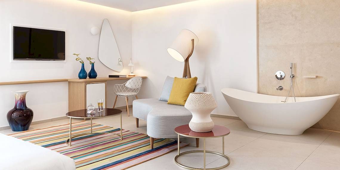 Innenansicht eines Zimmers im Myconian Kyma Hotel mit Badewanne, Fernseher, Couch und Tisch.