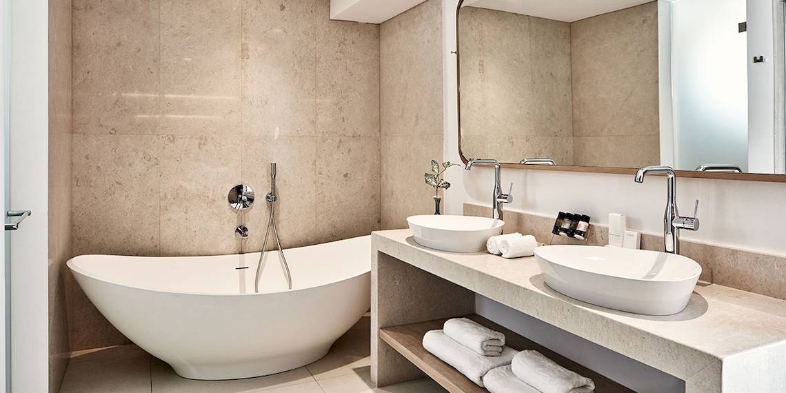 Das Badezimmer des Myconian Kyma Hotels mit einer Badewanne und zwei Waschbecken.