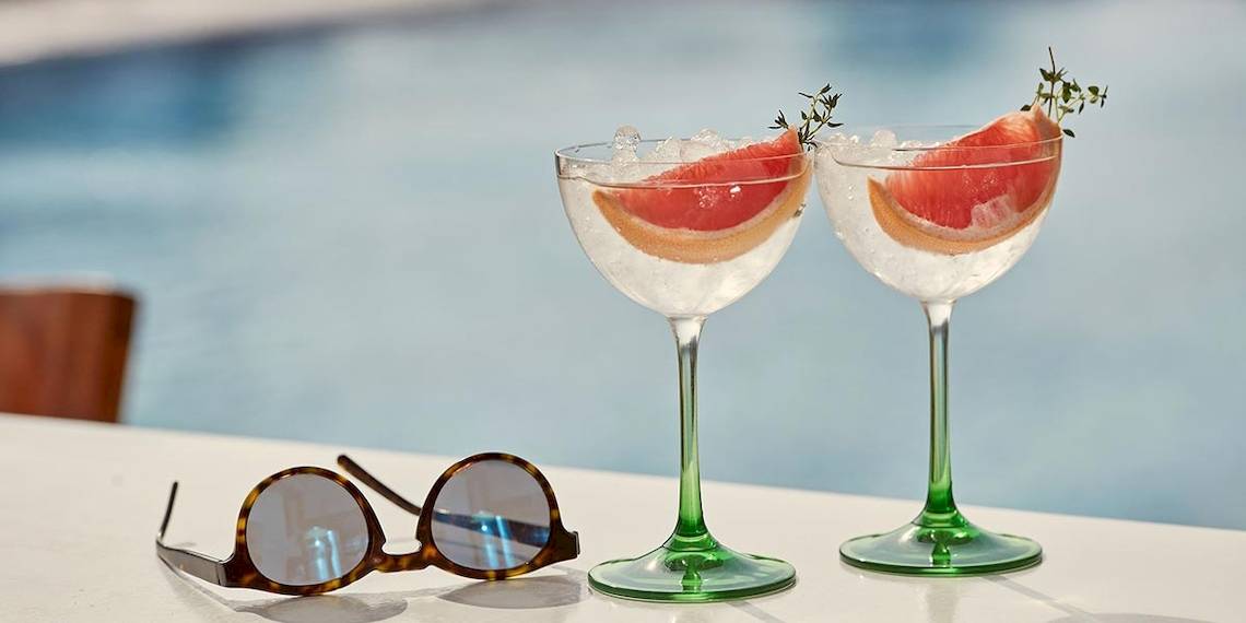 Zwei Gläser mit Gin und Tonic und einer Sonnenbrille auf einem Tisch am Pool